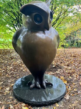 Image of owl made of bronze standing against a background of leaves and grass