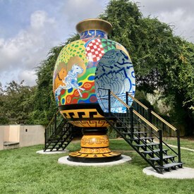 Image of large vessel shaped sculpture with stairs on either side leading up to an opening in the center of the vessel. The vessel itself is covered in colorful graffiti.