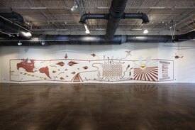 Mural across a cascading wall painted with brown clay slip depicting the Americas and the history of immigration to the present day.
