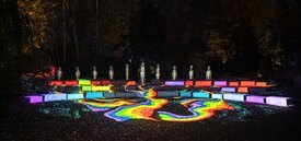 Image of Frog Head Rainbow. Rainbow light projections on the ground with rows of blocks also in rainbow colors.