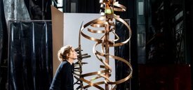 Image of woman sitting and looking at a sculpture of a tall bronze piece with twisting swirls from top to bottom