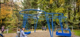 A large, blue abstract cloud-shaped sculpture with three traditional swings and two accessible swings set amongst trees.