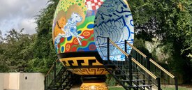 Image of large vessel shaped sculpture with stairs on either side leading up to an opening in the center of the vessel. The vessel itself is covered in colorful graffiti.