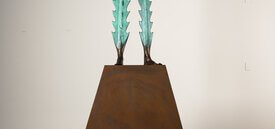 Two stalks of light green cacti with barbed edges morphing into two feet standing on a brown pedestal.