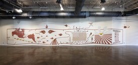 Mural across a cascading wall painted with brown clay slip depicting the Americas and the history of immigration to the present day.